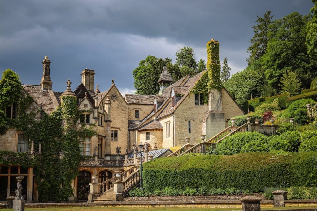 Scenic view of a historic manor house surrounded by lush green gardens in Castle Combe, England.
